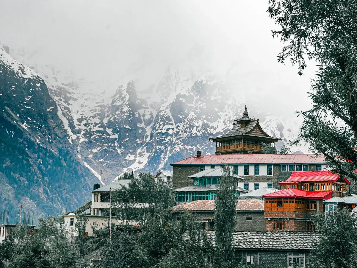 Snow-covered Himalayan peaks behind a temple village in Kalpa, Himachal Pradesh, on a cold, misty winter day