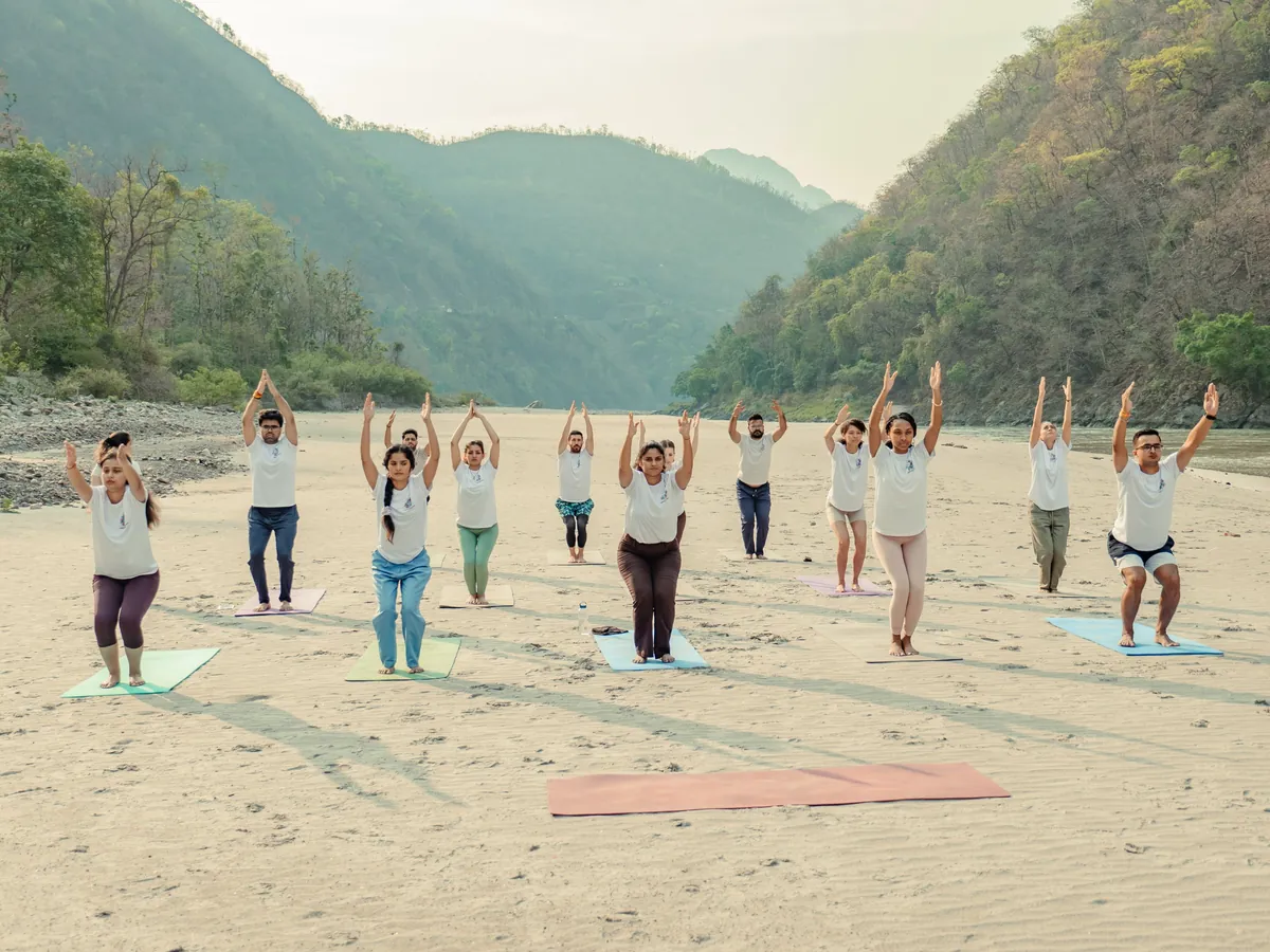 Students practising together on the sand beside the Ganga with the Rishikesh hills behind them